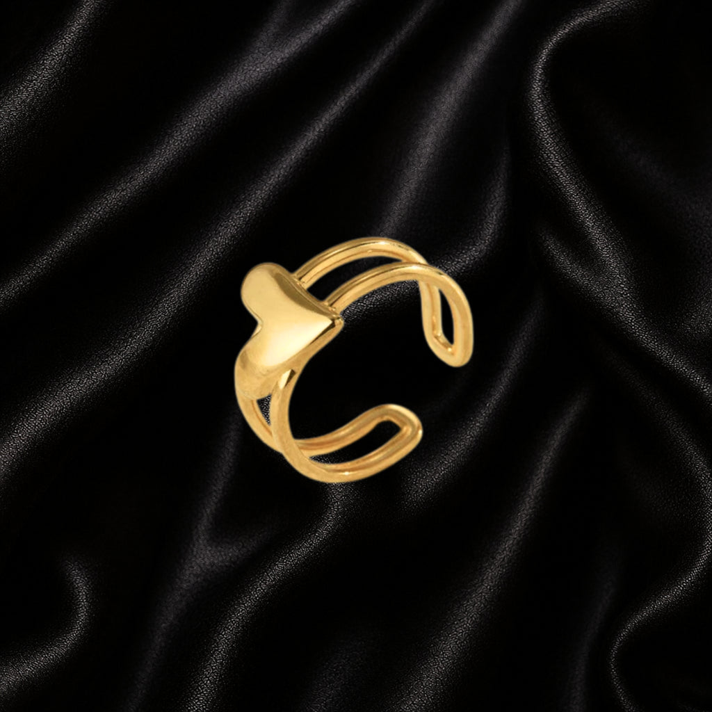 A gold-toned open cuff ring with a smooth, polished abstract curved design, displayed on a draped black satin fabric background.