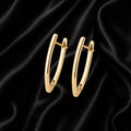 A pair of polished gold huggie hoop earrings displayed on a draped black satin fabric background.