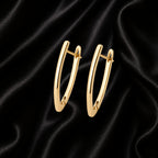 A pair of polished gold huggie hoop earrings displayed on a draped black satin fabric background.