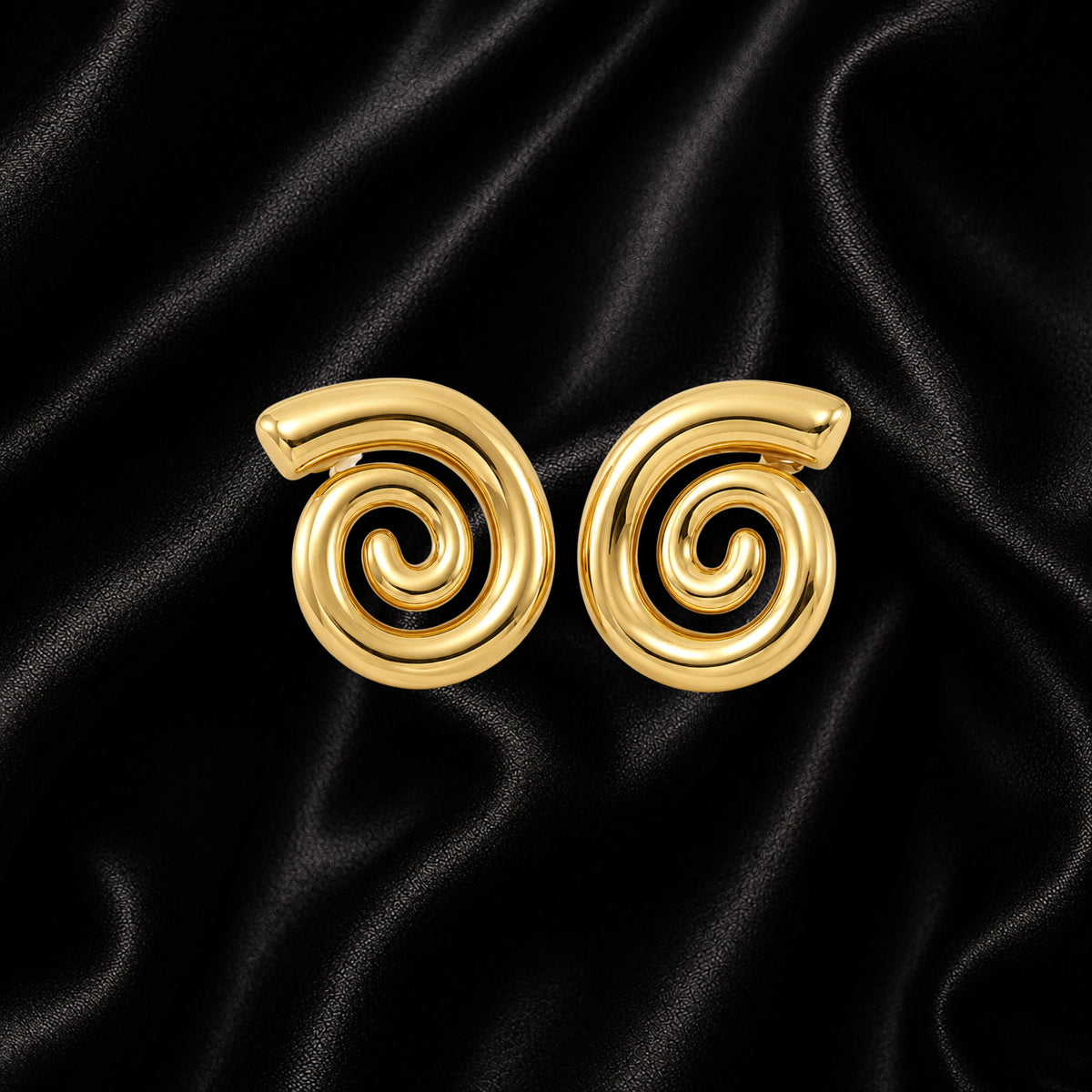A pair of gold spiral-shaped earrings displayed on a black satin fabric background.